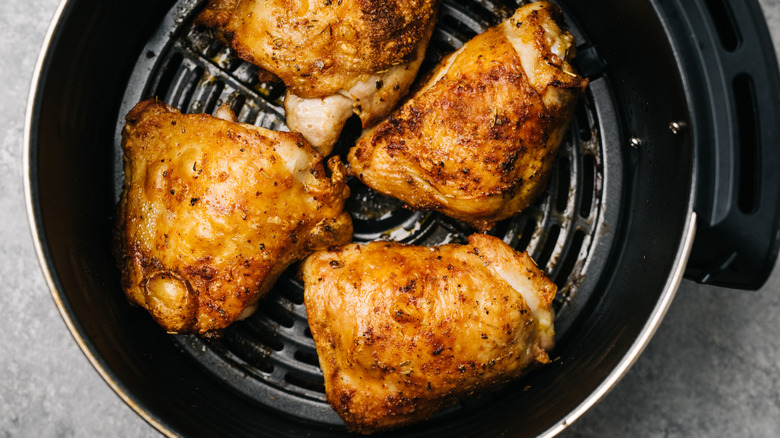 Four perfectly seasoned and cooked chicken thighs sitting in an open air fryer basket