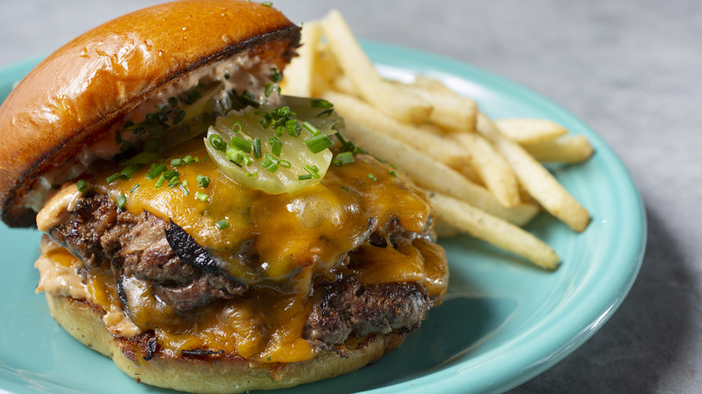 A juicy double burger with melted cheese and pickles on a brioche bun with fries