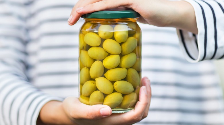 Hands holding a glass jar of green olives