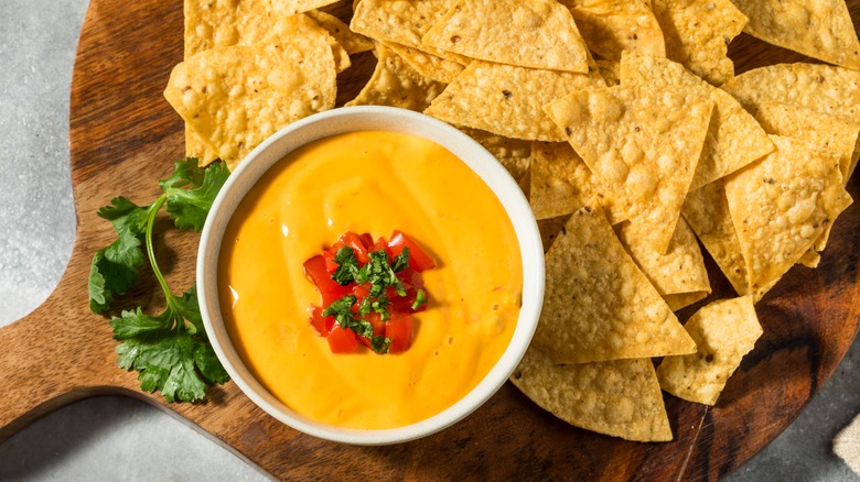 queso dip with tortilla chips on a wood cutting board