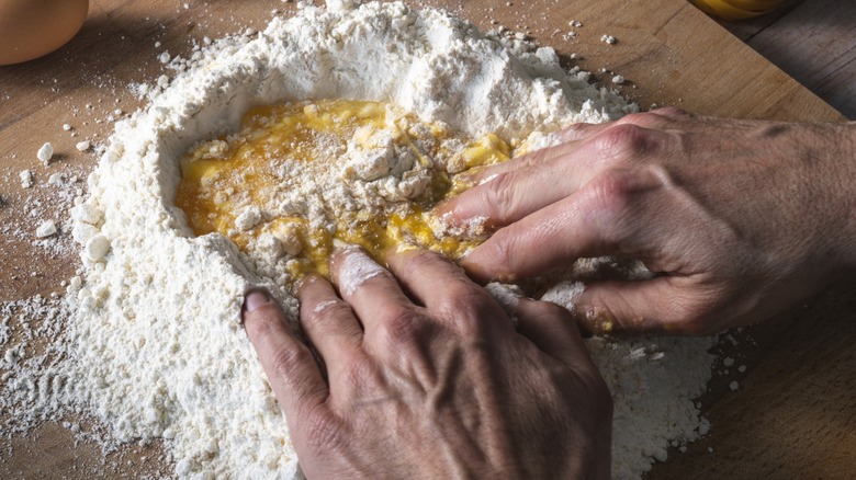 Hands kneading flour and eggs to make homemade pasta