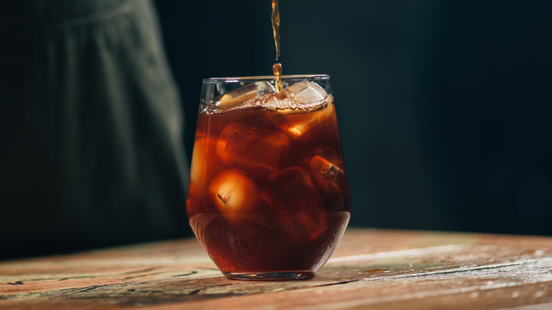 Small glass of cold brew coffee with ice cubes on wooden table