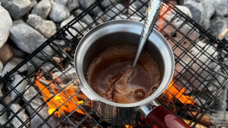 Pot of coffee simmering in metal saucepan on black grates over open fire