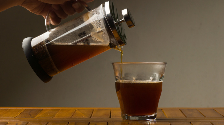 Hand pouring coffee out of French press into glass