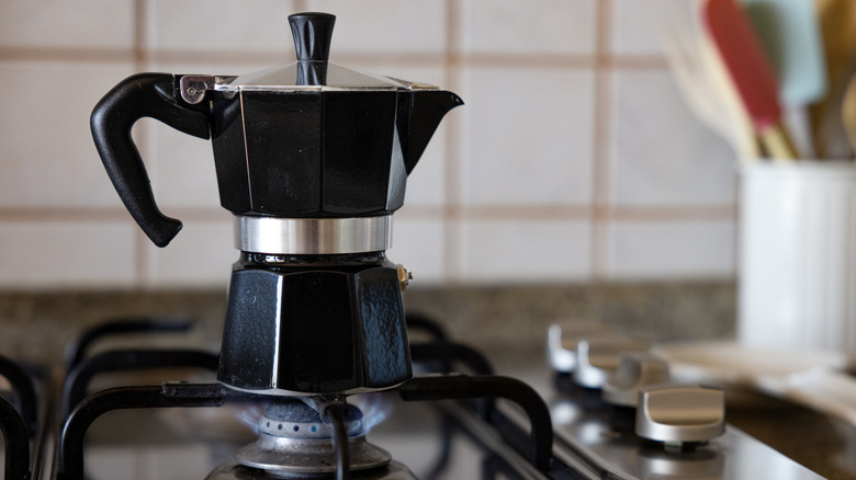 Black moka pot coffee maker over gas stovetop