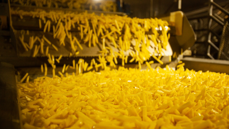 French fries falling from one conveyor belt onto another in a factory