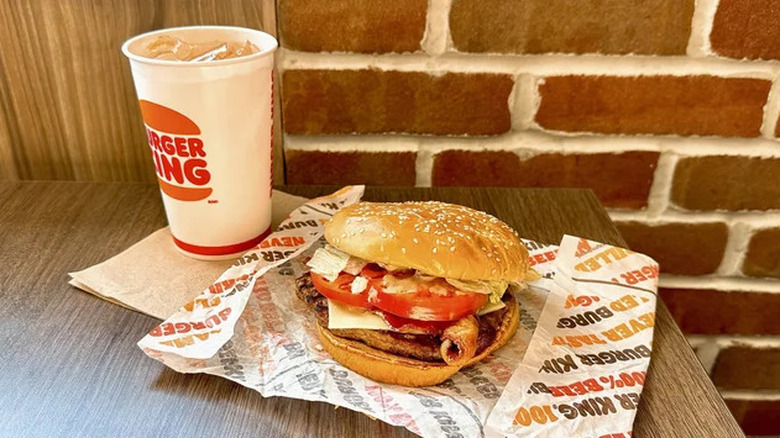 A Peppercorn BLT Whopper sitting on an open wrapper with visible lettuce, tomato, sauce, cheese, and bacon, next to a drink