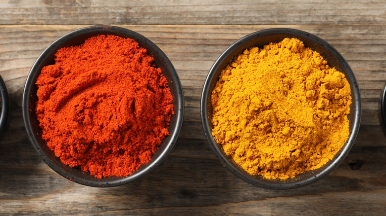 bowls of turmeric and paprika powder on wood background
