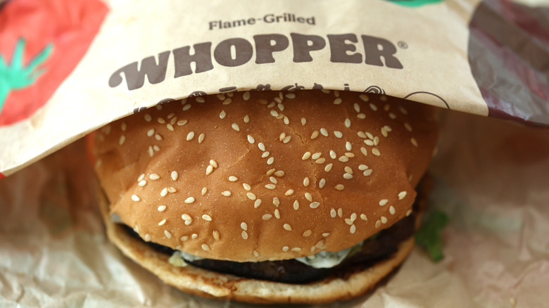 A Burger King Whopper half exposed under the paper showing off the Sesame Seed bun
