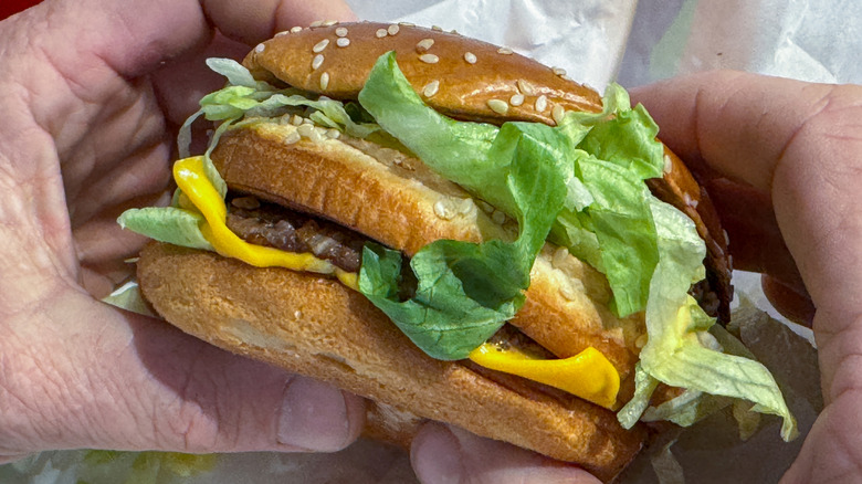 Two hands holding a Big Mac above its paper wrapping