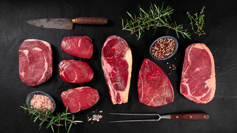A selection of different cuts of beef with herbs and knife