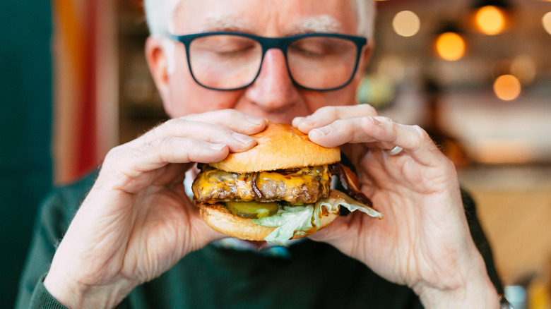 Gray-haired foodie eating a fast food burger