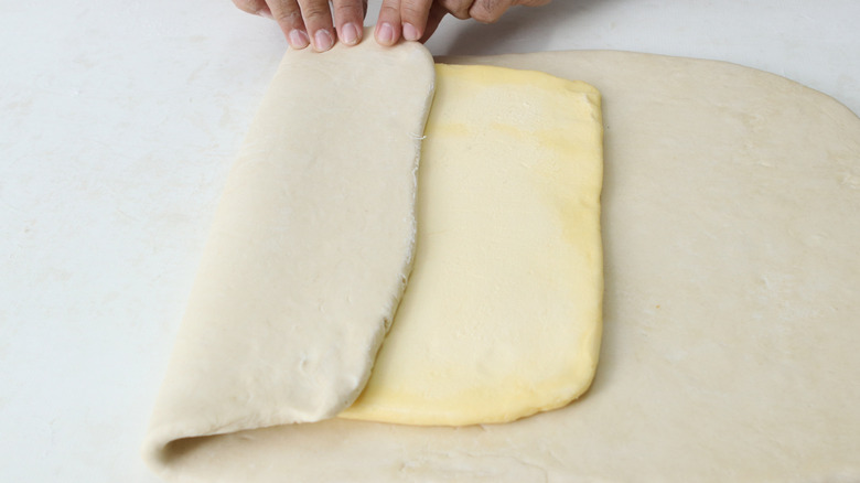 Overhead view of person laminating croissant dough with sheet of butter