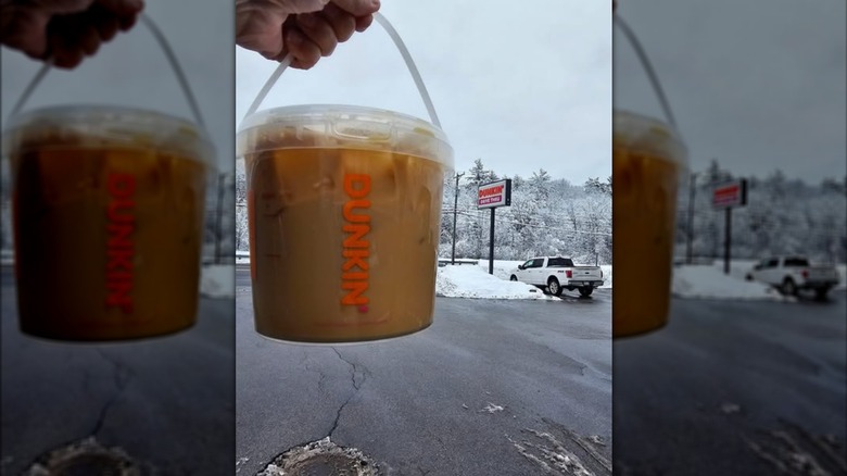 Hand holding Dunkin' iced coffee bucket in parking lot