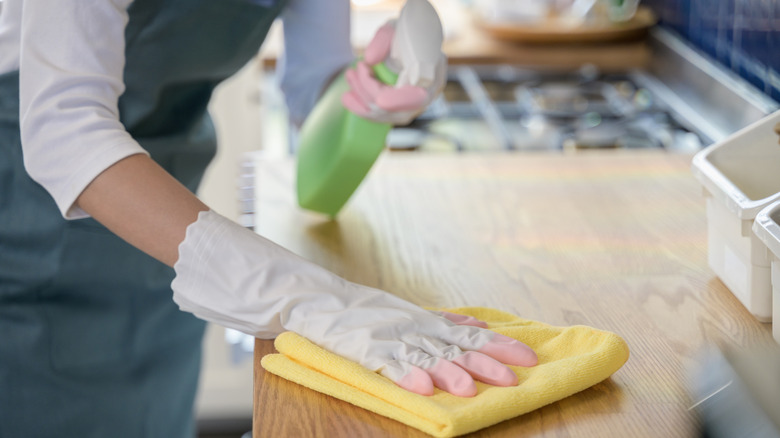 Gloved hands cleaning kitchen counter with cloth