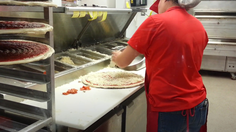 Costco employee sprinkling cheese on pizza