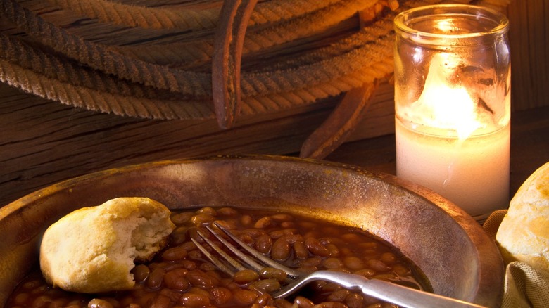 A pan of cowboy beans and biscuits besides a candle in a jar