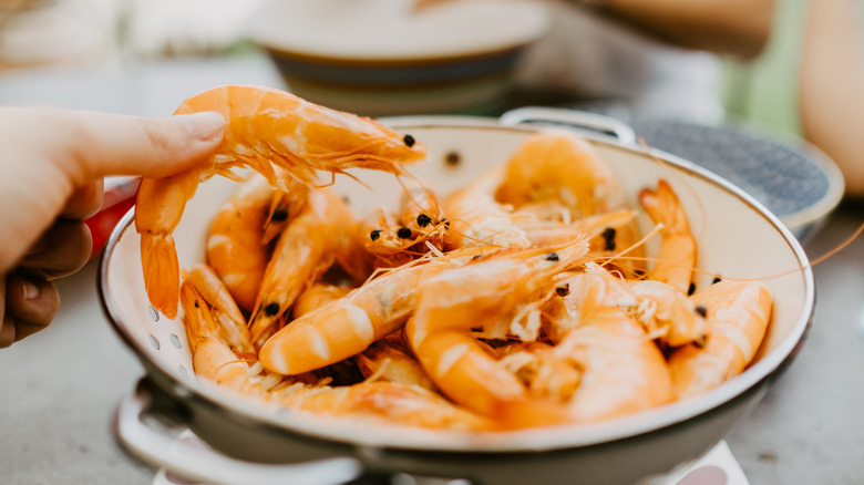 Someone picking a pink shrimp out of a bowl of other shrimps all with heads and tails still attached