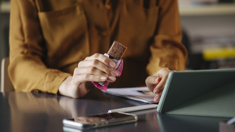 woman's hand working at desk holding open protein bar
