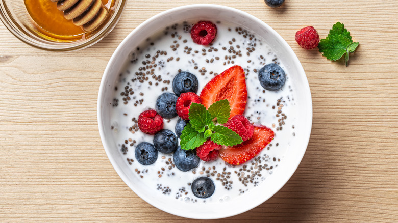chia seeds in yogurt bowl with berries, mint leaves, and some honey in a bowl beside