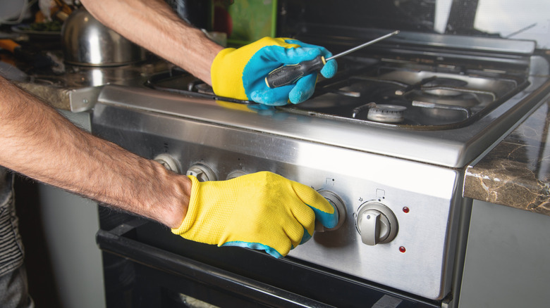 Man wearing gloves repairs kitchen oven
