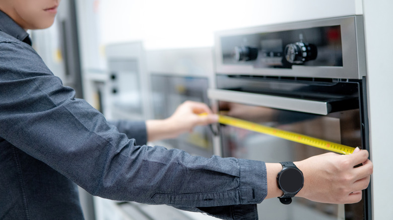 Close-up of a man using a measuring tape to determine the width of an oven in an appliance store