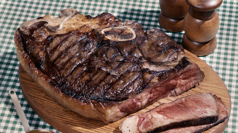 A 1960s porterhouse steak on a wooden cutting board atop a green gingham tablecloth