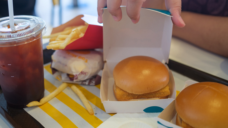 Black tray holding two McDonald's Filet-O-Fish sandwiches, sleeve of fries, and drink cup with hand opening box containing Filet-O-Fish