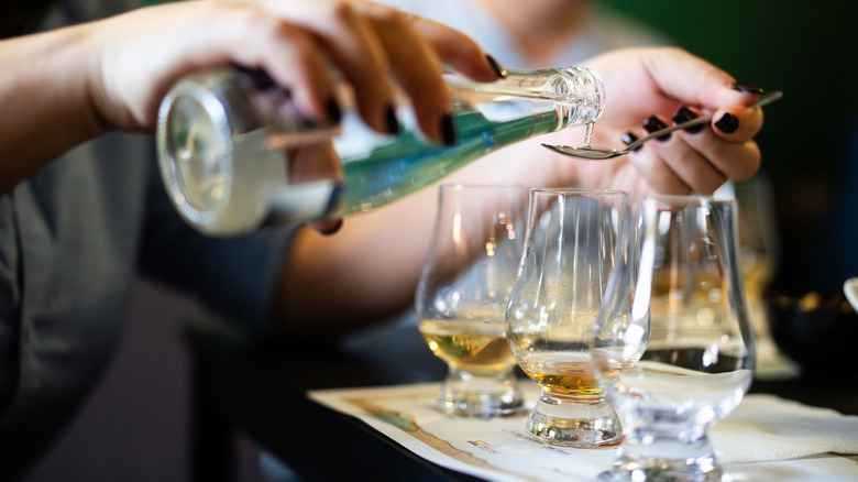 Person carefully adding a spoonful of water to glasses of Scotch