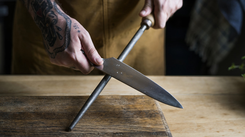 person with tattooed hand sharpening a kitchen knife on a steel