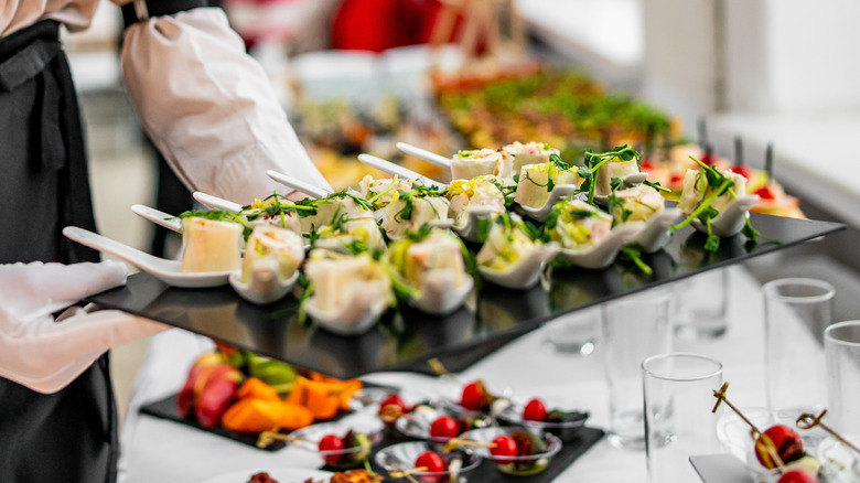 A server replenishes a platter of canapes at a buffet table.