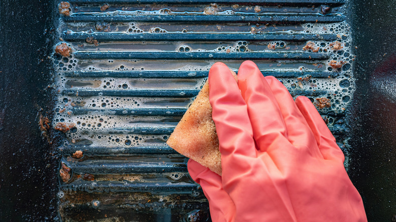 Cleaning a grill with sponge in pink rubber gloves