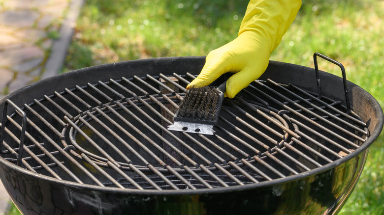 Person wearing gloves and scraping grill grates with a grill scraper