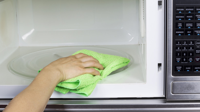 A person using a green microfiber cloth to clean the interior of a microwave