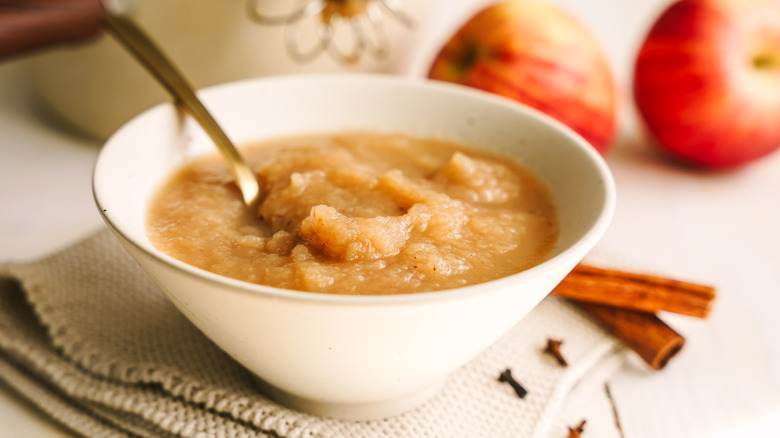 Dish of pureed applesauce surrounded by whole apples