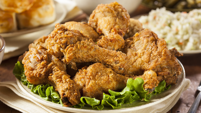A plate of homemade fried chicken on a kitchen table with biscuits and coleslaw