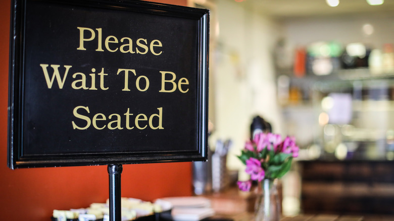 A "Please Wait To Be Seated" sign at the host stand of a restaurant