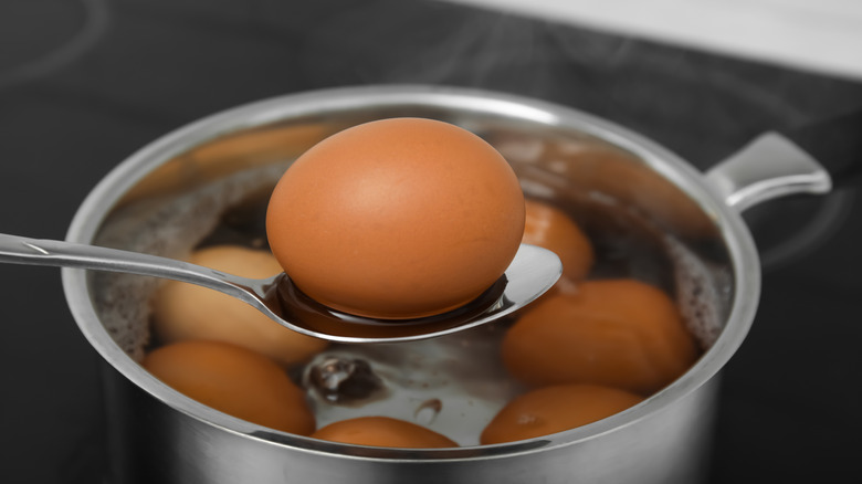 An egg in a spoon held over a pan filled with water and eggs