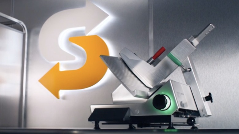 A stainless steel deli slicer with Subway logo in background