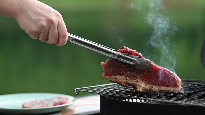 Hand using tongs tap steak