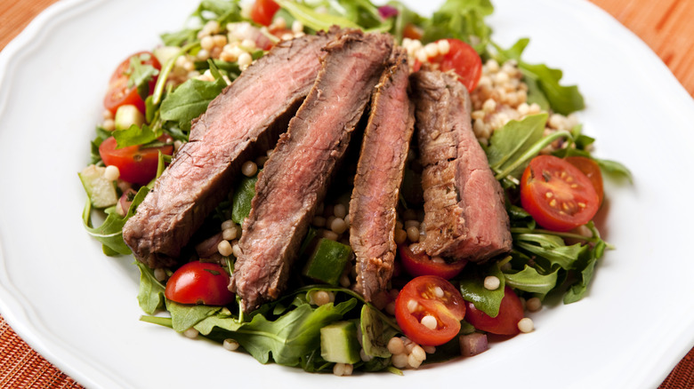 Green salad with sliced steak, cherry tomatoes, and quinoa
