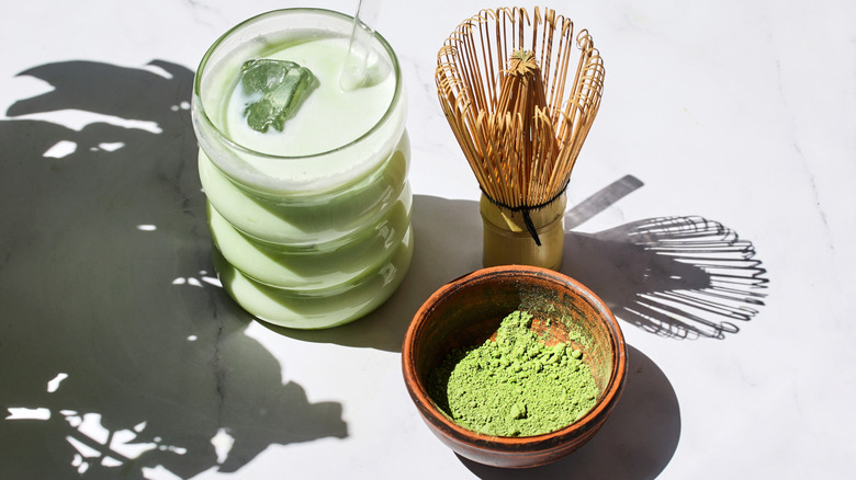 Iced matcha drink next to whisk and matcha powder