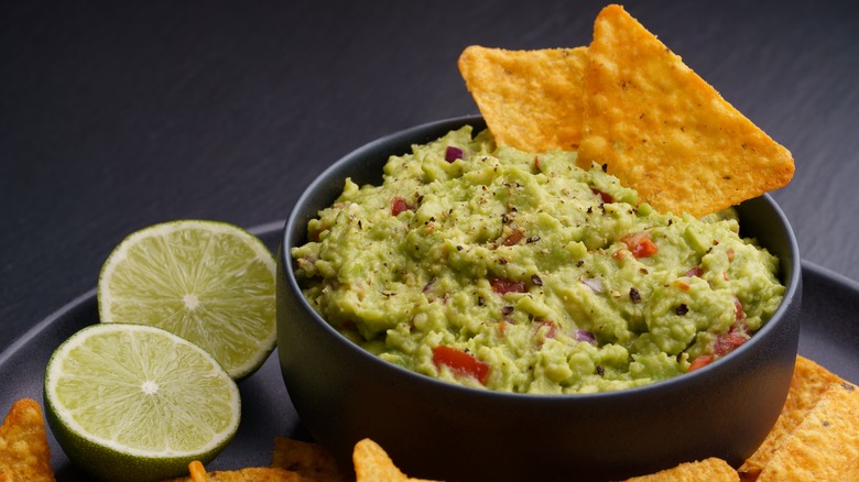 bowl of guacamole with chips and limes