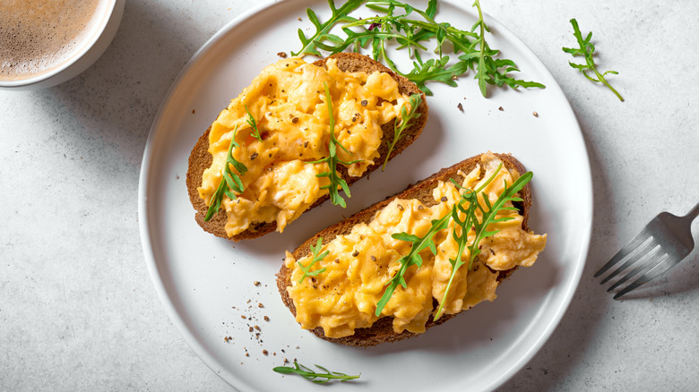 Scrambled eggs served on toast with fresh arugula