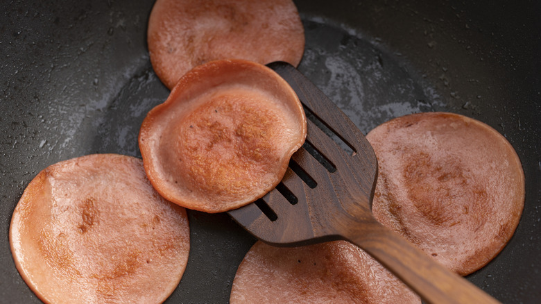 Spatula flipping bologna in a frying pan