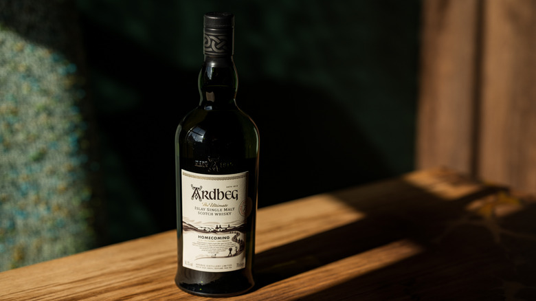 A bottle of Ardbeg Homecoming on a wooden board in a shadowy room
