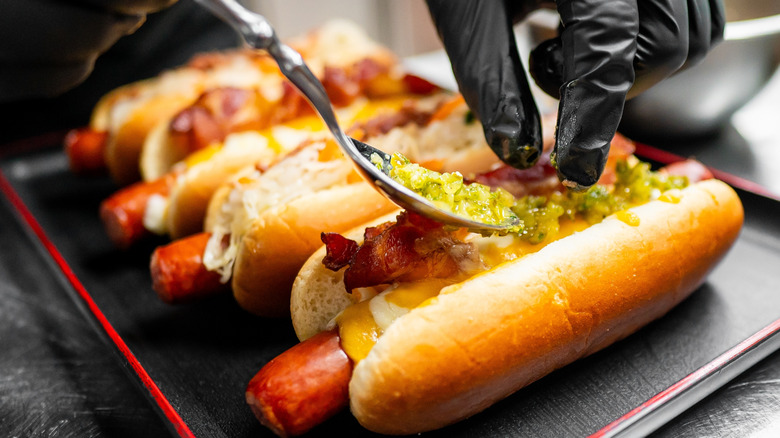 person with black glove adding toppings to hot dogs