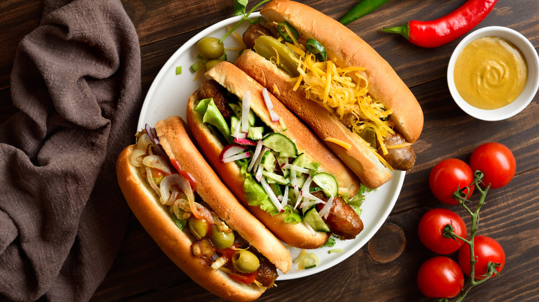 Betrayal of hot dogs on a white plate, each top differently with various vegetables, sauces, and more