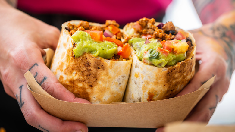 hands holding half a burrito filled with guacamole