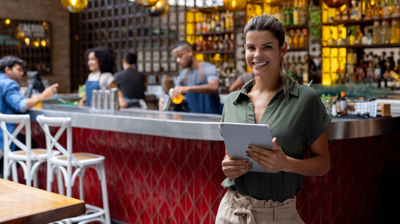 Restaurant hostess with tablet smiling in front of bar